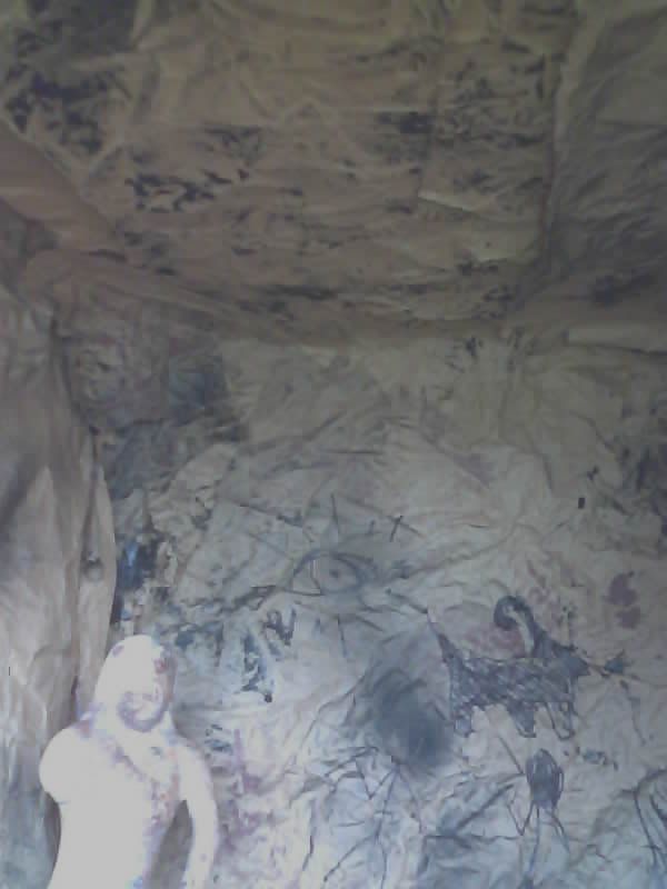 Saved camera frame: a pale carved figure standing at the foot of a painted cave wall.